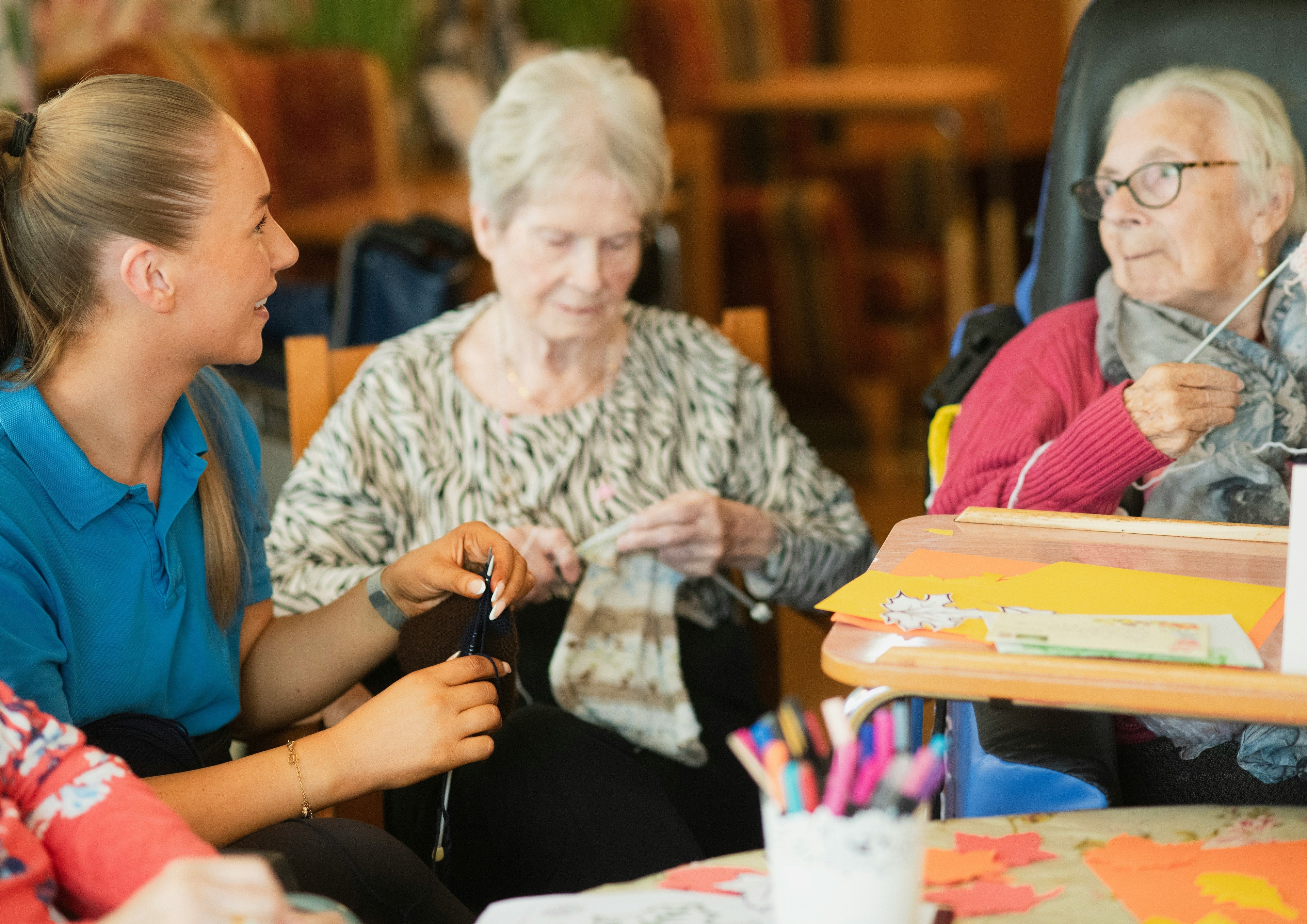 Aged care worker with brown hair does craft with two older women