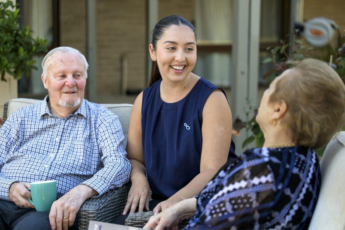 Young aged care worker sitting with and conversing with an older man and an older woman